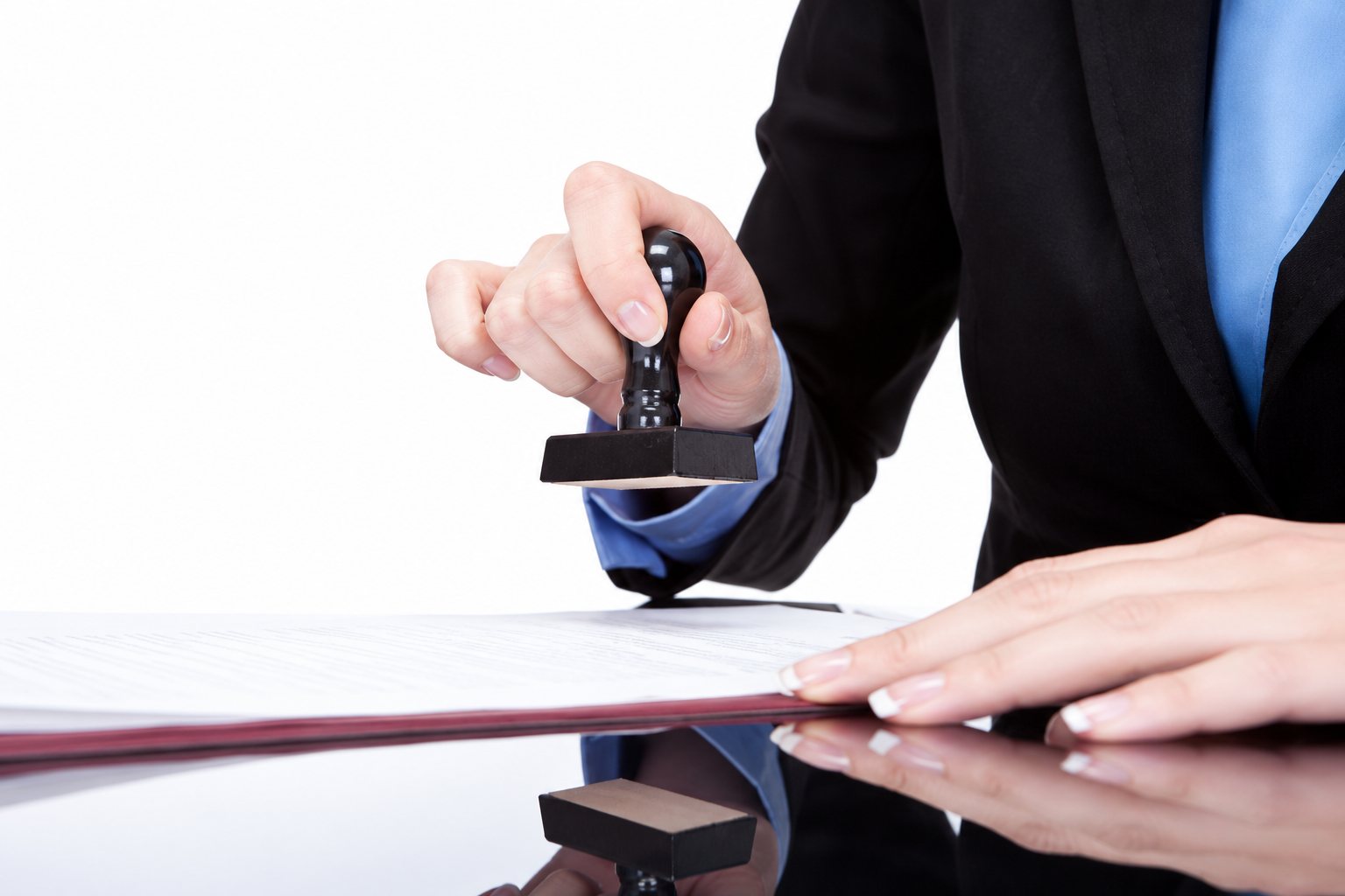 Une personne en tailleur sombre appose un tampon sur un document posé sur une table brillante.
