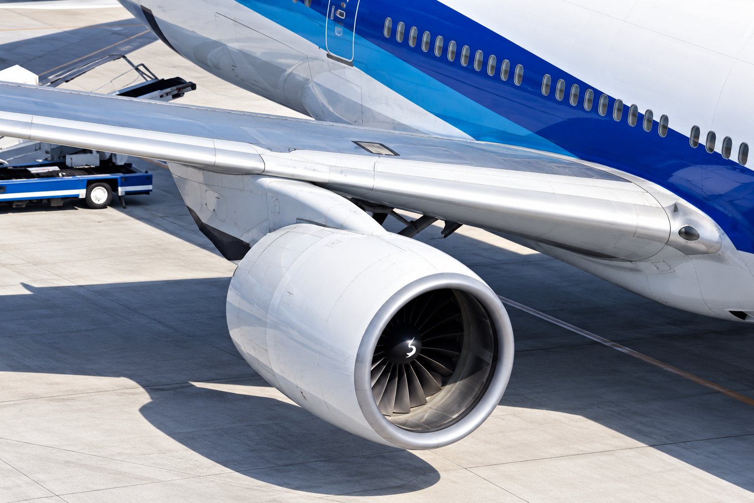 Vue rapprochée du réacteur et de l'aile d'un avion de ligne blanc et bleu stationné sur le tarmac d'un aéroport.