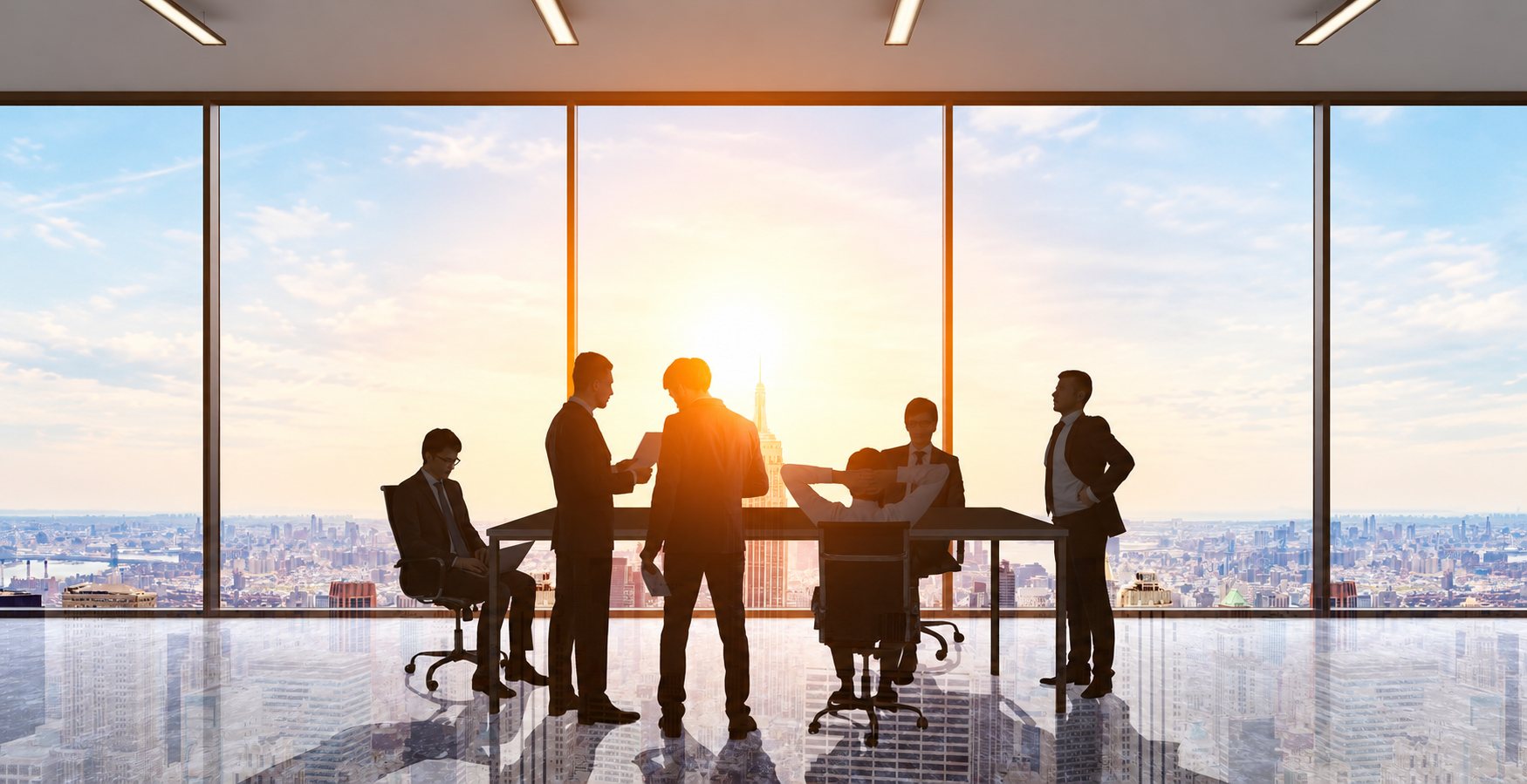 Des hommes d'affaires en silhouette se réunissent autour d'une table dans un bureau en hauteur, face à une vaste baie vitrée donnant sur une ville au soleil couchant.
