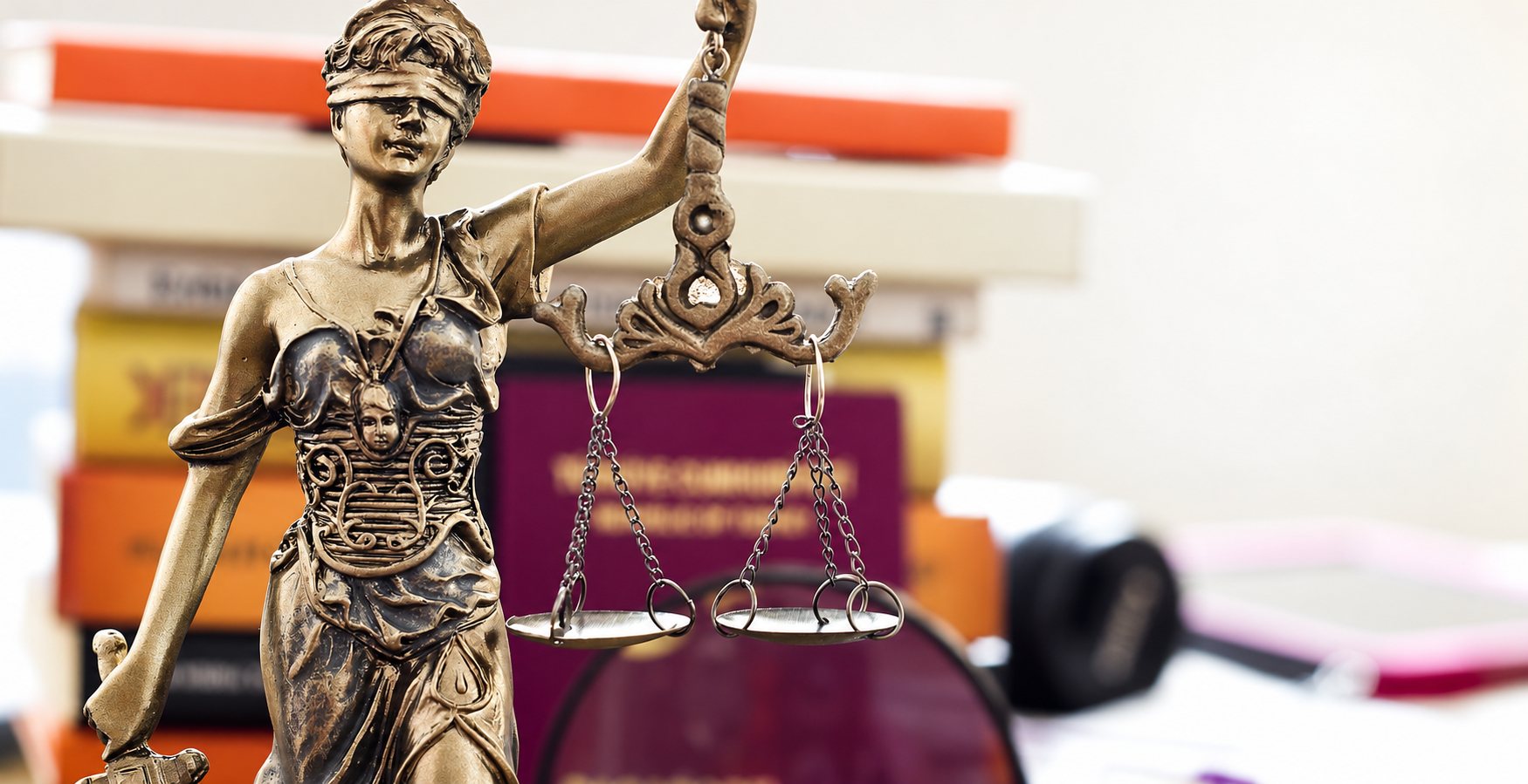 Une statuette en bronze de la justice, les yeux bandés, tient une balance devant une pile de livres juridiques floue.
